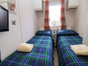 Una habitación pequeña con dos camas, una mesita de noche, un espejo y una ventana con cortinas.