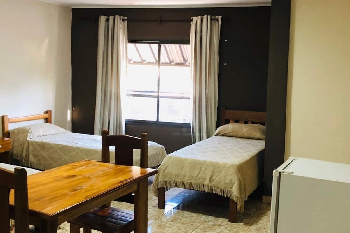 A room with two beds, a wooden table, and a refrigerator.