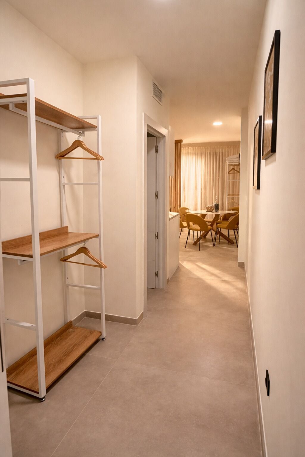 Un pasillo con un armario blanco, un comedor con mesa y sillas, y una puerta que da a otra habitación.