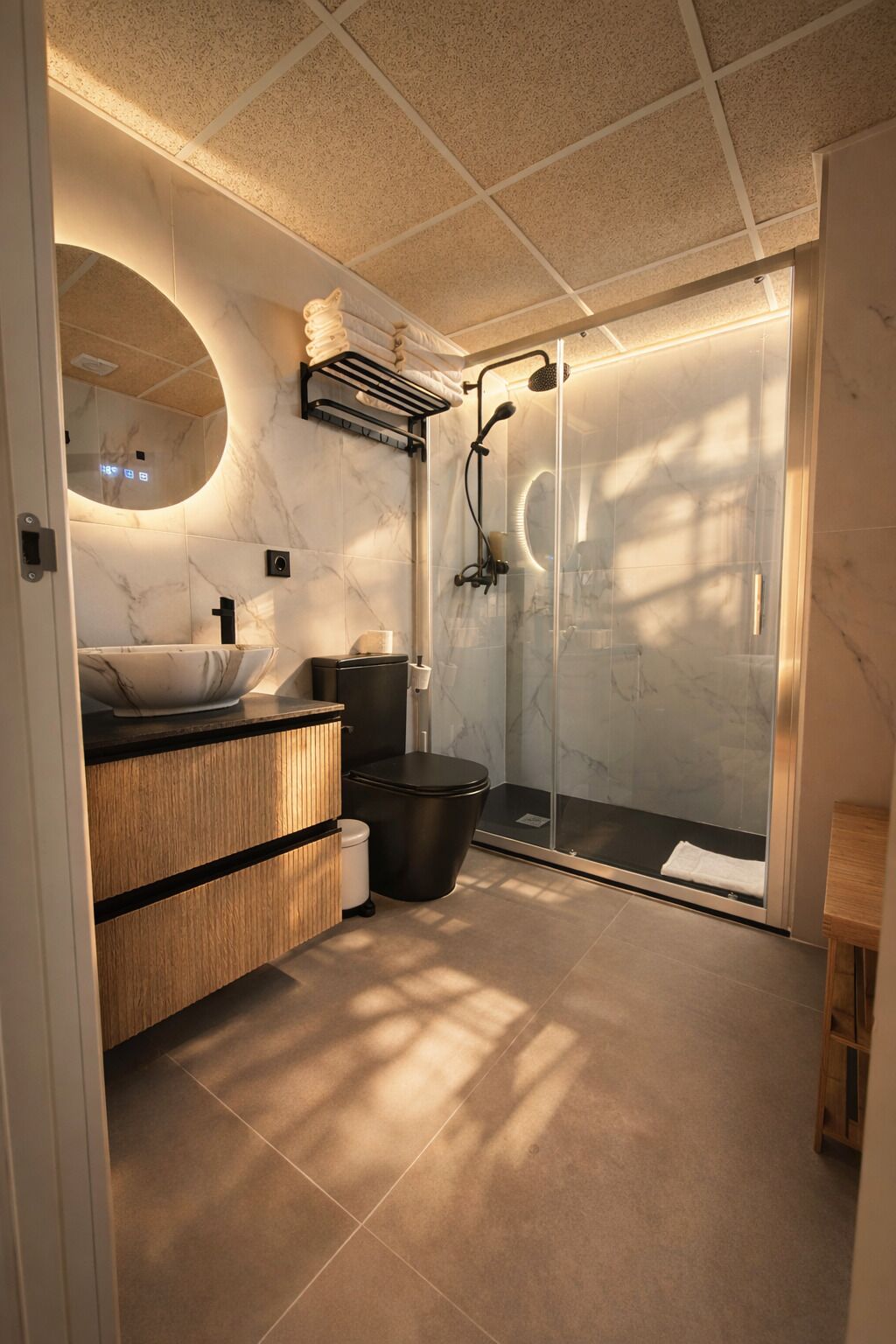 Un baño moderno con tocador de mármol, cabina de ducha con mampara de vidrio y un mueble de madera.