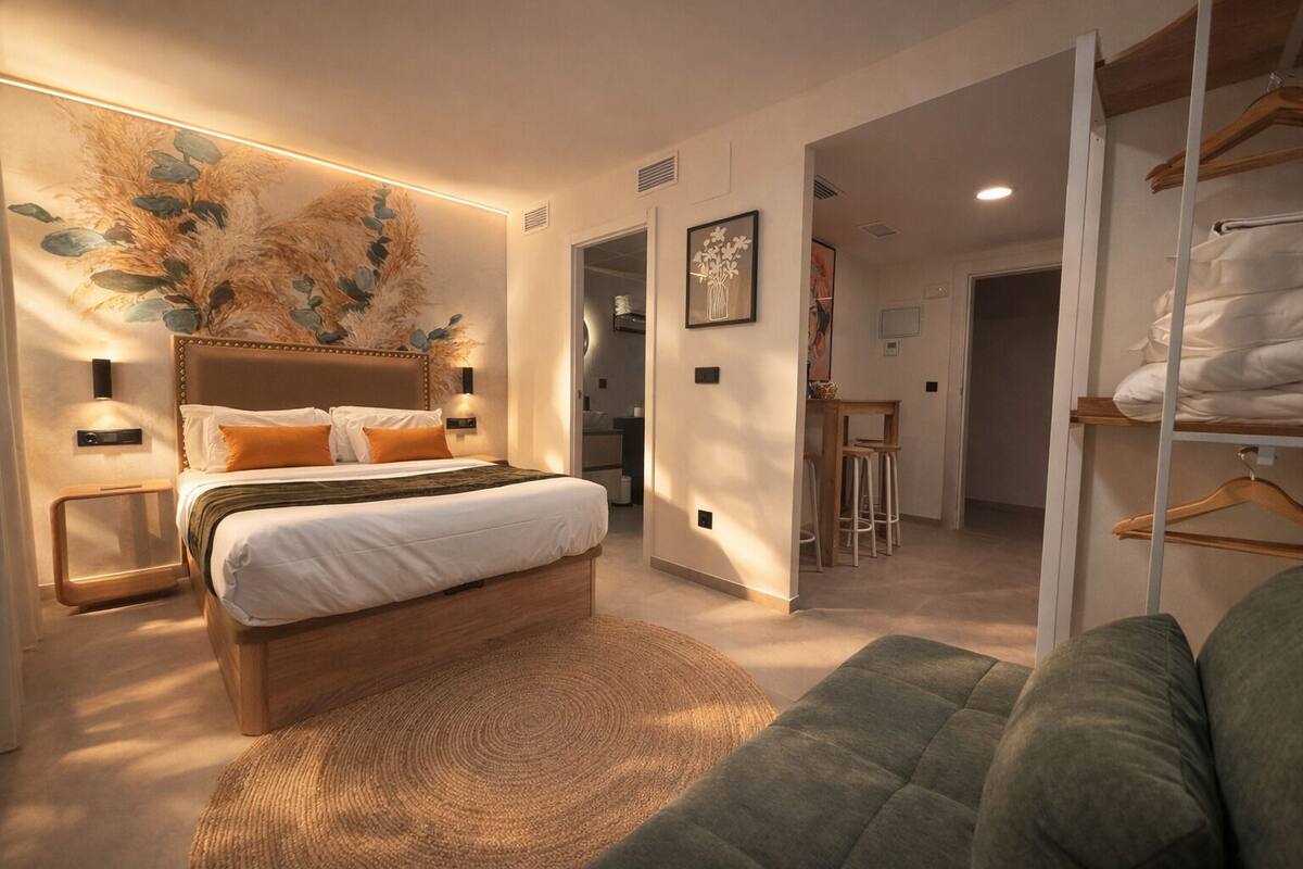 A modern bedroom with a large bed, bedside tables, a wall-mounted lamp, and a view into the adjacent dining area.