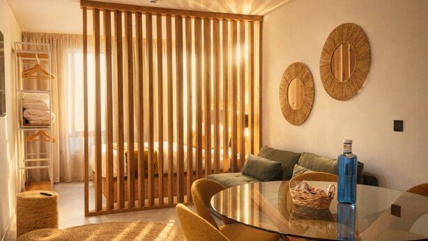 Una sala de estar moderna con una mesa de centro de vidrio, sillas color mostaza, un tapete tejido y una partición de madera.