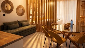 Una sala de estar moderna con un sofá, una mesa de comedor de vidrio con sillas, un separador de madera y espejos montados en la pared.