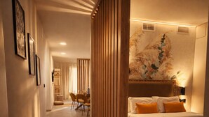 Habitación de hotel con cama, un ventanal con vistas, una separador de madera y un pasillo que conduce a otra habitación.