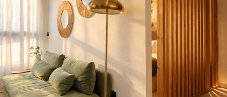 A room with a green sofa, a floor lamp, and two wall mirrors.