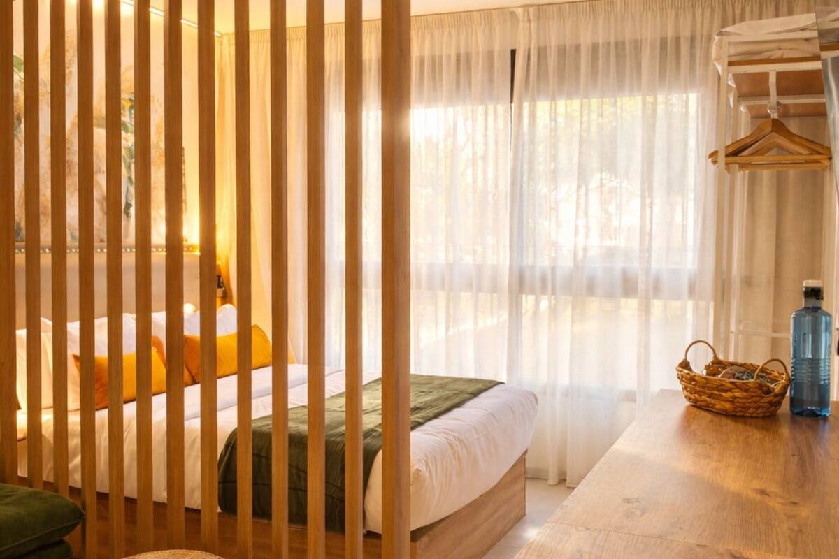 A bedroom with a bed, a wooden partition, a table, and a hanging rack.