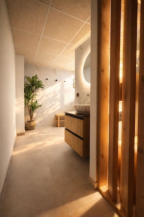 A modern bathroom with a marble wall, a wooden cabinet, and a potted plant.