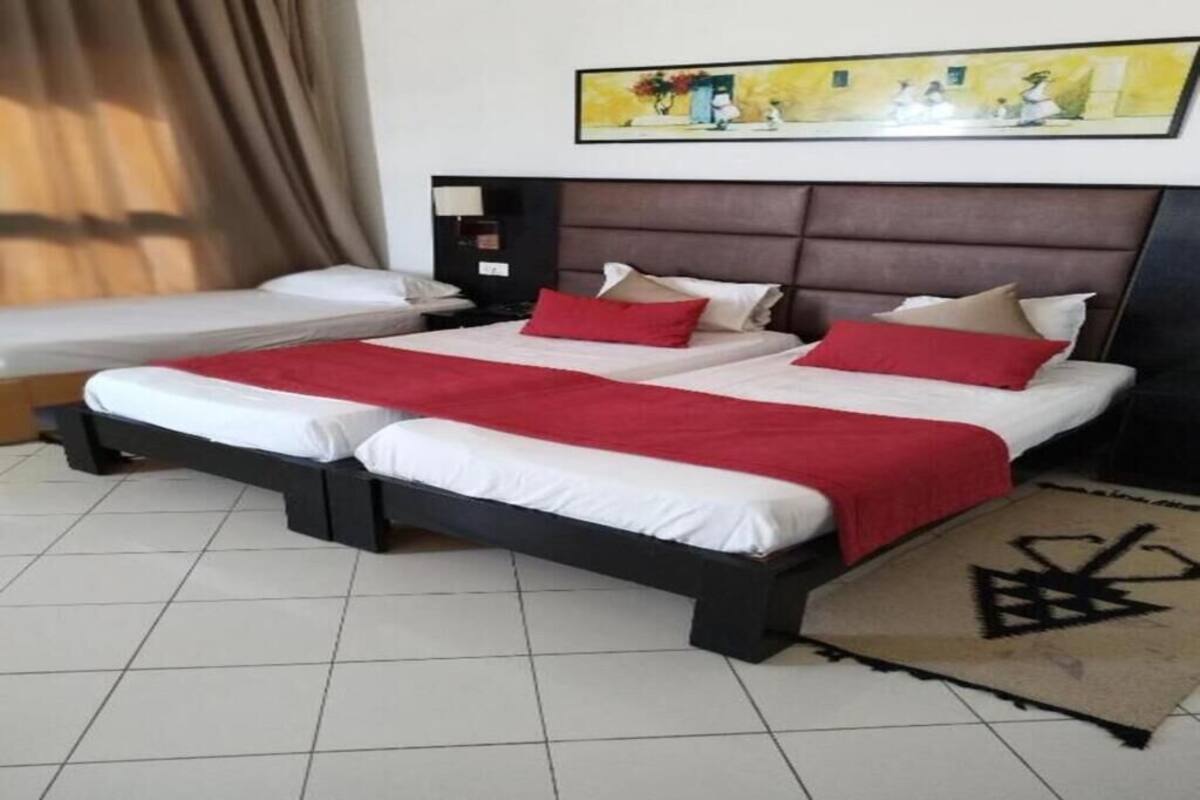 A hotel room with two beds, a headboard, a painting on the wall, and a tiled floor.