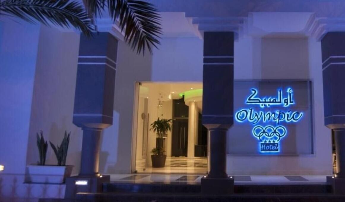 En hotelindgang med en neonskilte, der viser 'Olympic Hotel'.