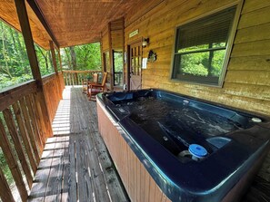 Eine Holzjagd-Hütte mit Whirlpool auf der Veranda, einer Holzterrasse und Blick auf den Wald.