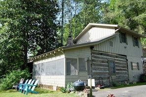 A cabin with a large windowed porch, a stone chimney, and a grill outside. - Historic Two-story Riverside Cabin w/Hot Tub in Gatinburg (Gatlinburg)