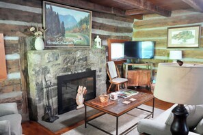 A rustic cabin interior with a stone fireplace, wooden walls, a television, and a comfortable seating area. - Historic Two-story Riverside Cabin w/Hot Tub in Gatinburg (Gatlinburg)