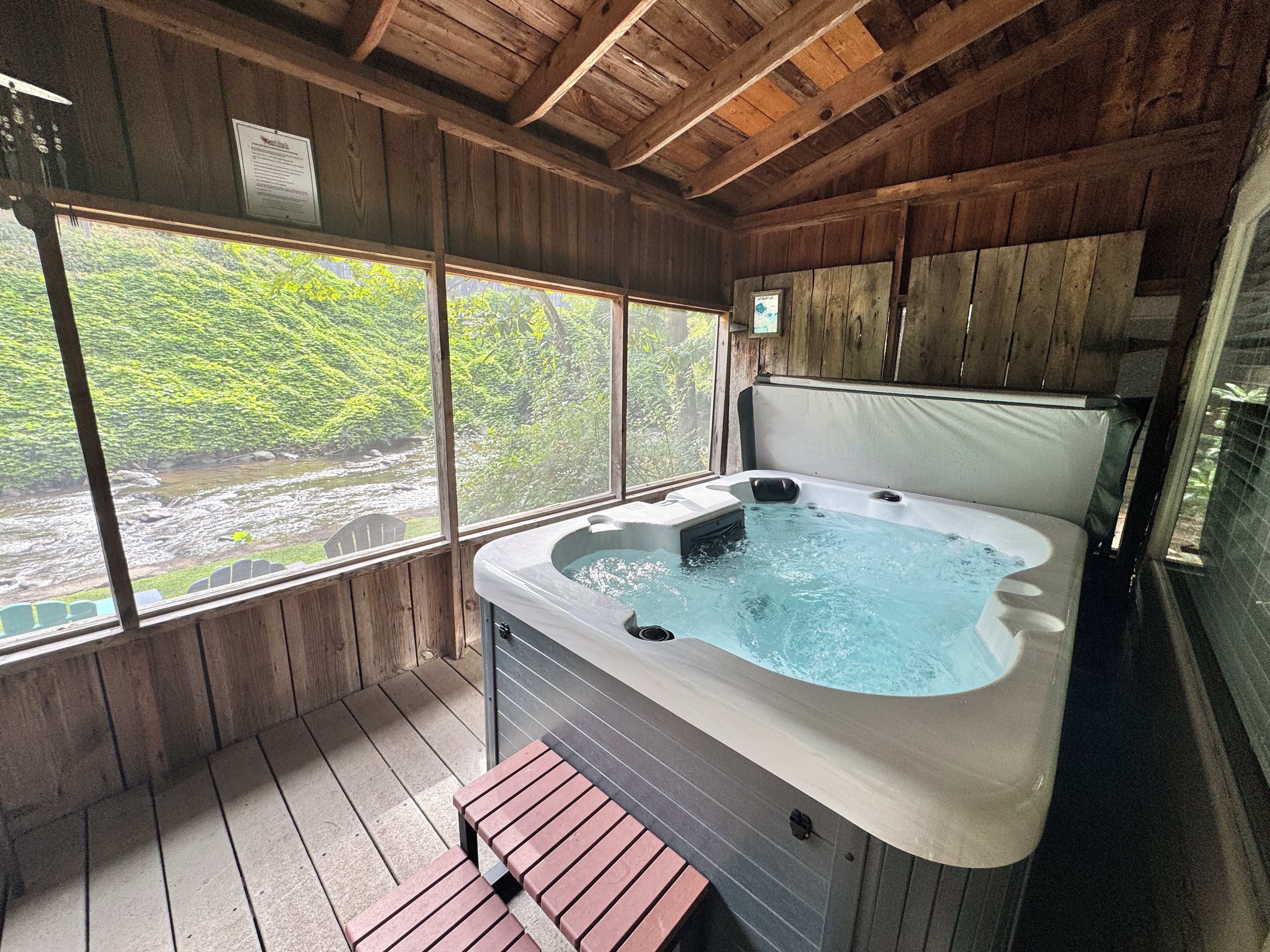 A wooden cabin with a hot tub and a view of a river.