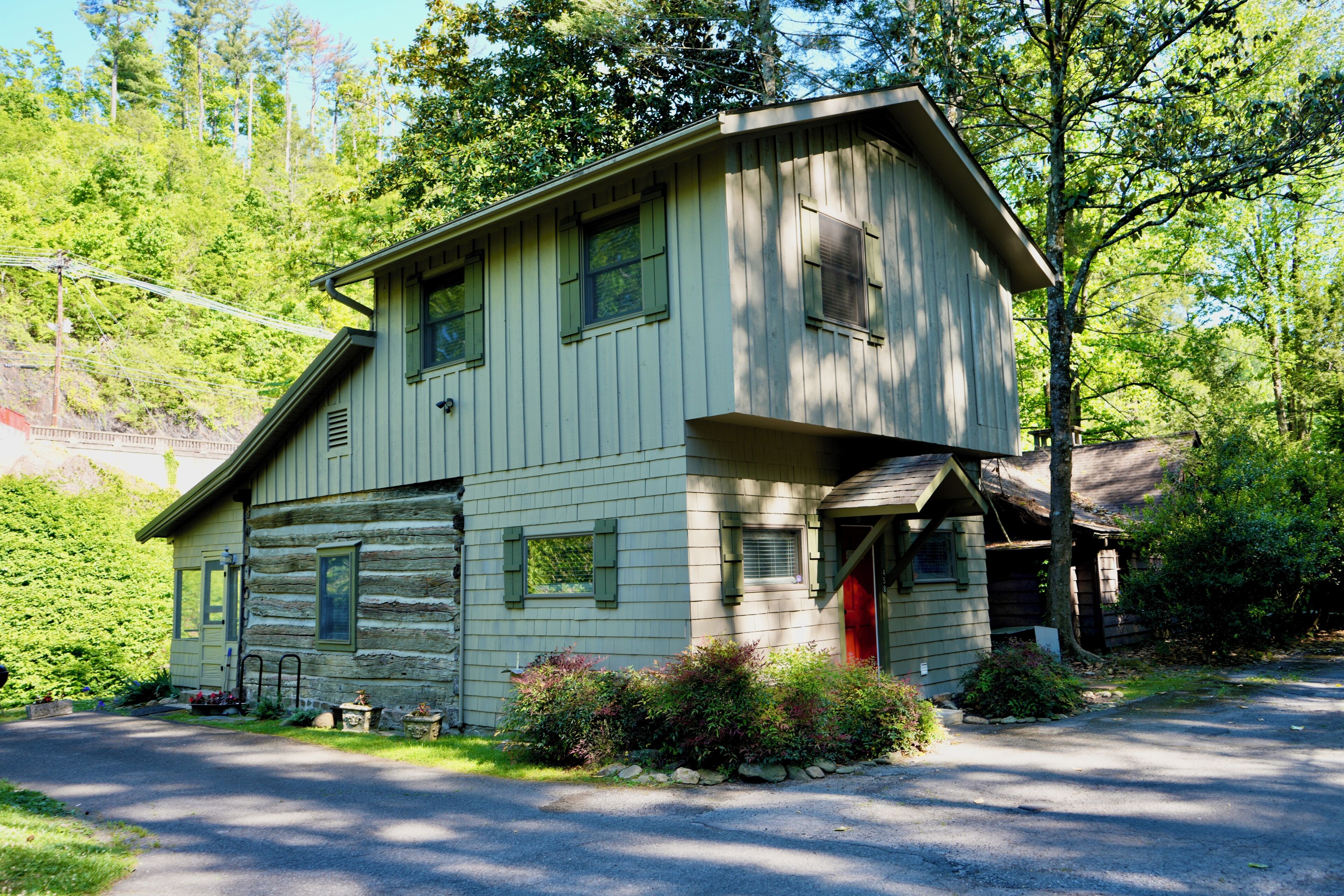 A log cabin with a front porch, a garage, and a red door.