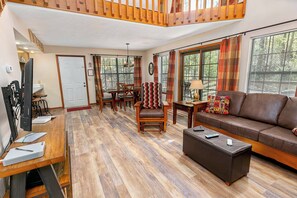 A spacious living room with a wooden floor, a brown leather sofa, a dining table with chairs, and a staircase. - Hot Tub | Fireplace | Game Room | Pool Access (Gatlinburg)