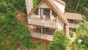 Une cabane à deux étages dotée d’un balcon, entourée d’une forêt dense.