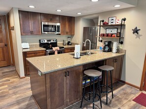 A kitchen with wooden cabinets, a granite countertop, a stainless steel refrigerator, a microwave, a stove, and a coffee maker. - Hot Tub | Fireplace | Game Room | Pool Access (Gatlinburg)