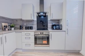 Una cocina moderna con armarios blancos, horno empotrado, microondas y cafetera.