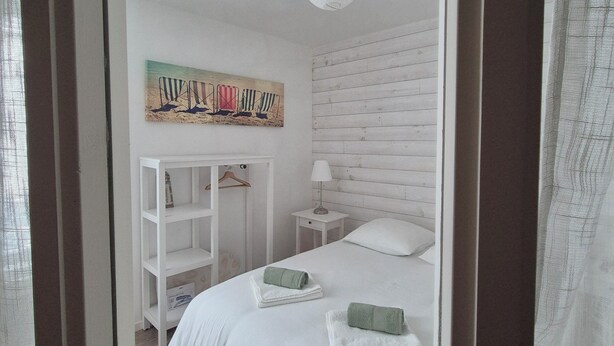 A bedroom with a white bed, a nightstand, a lamp, a shelf, and a painting on the wall. - Old fisherman's cottage completely renovated (Étel)