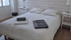 A bedroom with a white bed, two bedside tables, a window with curtains, and a wooden floor. - Old fisherman's cottage completely renovated (Étel)
