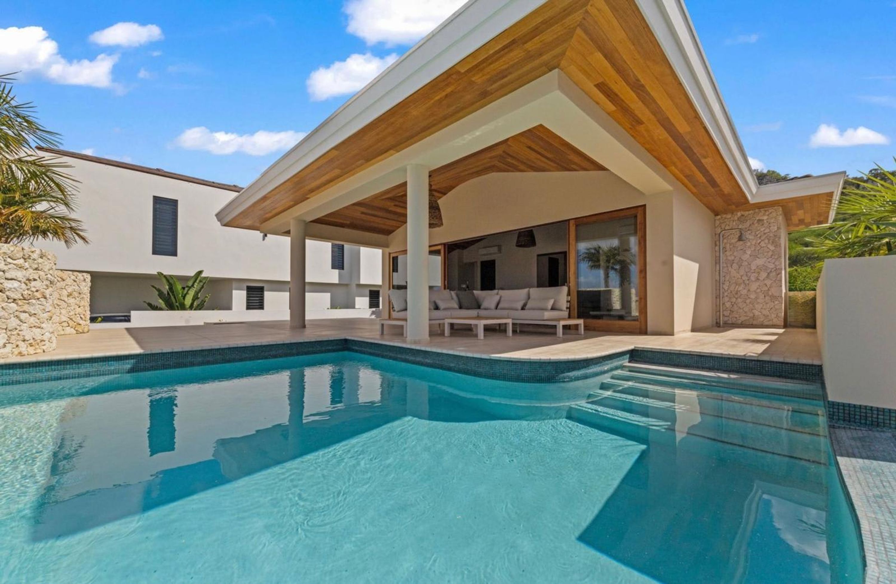 A modern house with a swimming pool, a covered patio, and a stone wall.