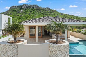 A modern house with a swimming pool, stone walls, and a view of a mountain. - NEW 4BR Villa With 2 Pools at Blue Bay (Sint Michiel)