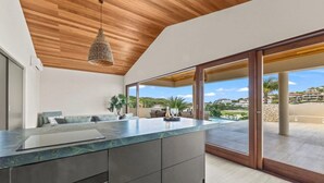 A modern kitchen with a large island, wooden ceiling, and a view of a pool and landscape. - NEW 4BR Villa With 2 Pools at Blue Bay (Sint Michiel)