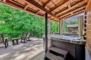 A wooden deck with a hot tub, outdoor seating, and a view of a house through a window. - Riverfront | Dog Friendly | Close to GSMNP (Townsend)
