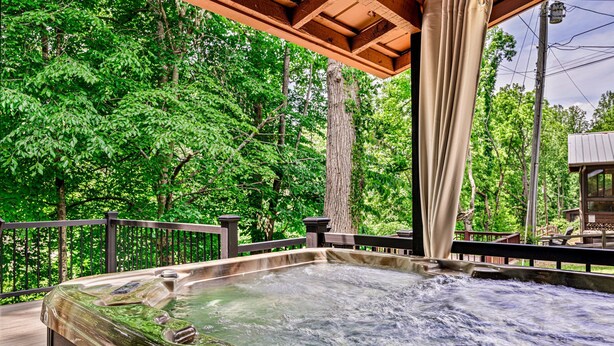 Ein Whirlpool mit einer Holzterrasse und Geländer, umgeben von üppigen, grünen Bäumen.