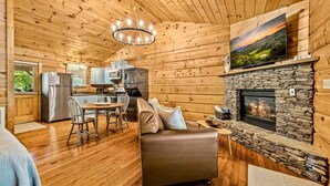 Ein gemütliches Blockhaus-Interieur mit Kamin aus Stein, Holzwänden, einem Essbereich und einem Wohnzimmer mit Sofa.