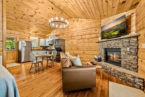 A cozy cabin interior with a stone fireplace, wooden walls, a dining area, and a television mounted above the fireplace. - Riverfront | Dog Friendly | Close to GSMNP (Townsend)