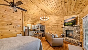 Ein Blockhaus-Interieur mit einem Bett, einem Kamin, einer Essecke und einer Küche.