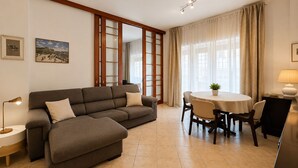 A modern living room with a sofa, a dining table with chairs, a lamp, and a view through a window with curtains. - Cozy apartment in Talenti - Well connected and quiet" (Roma)
