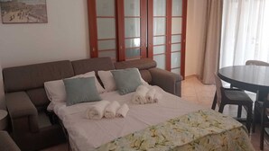 A hotel room with a sofa bed, a small table, a dining table, and a large window with curtains. - Cozy apartment in Talenti - Well connected and quiet" (Roma)