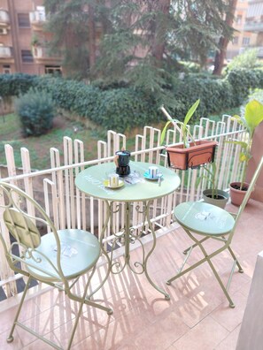 A balcony with two metal chairs, a small round table, and a hanging planter with a potted plant.