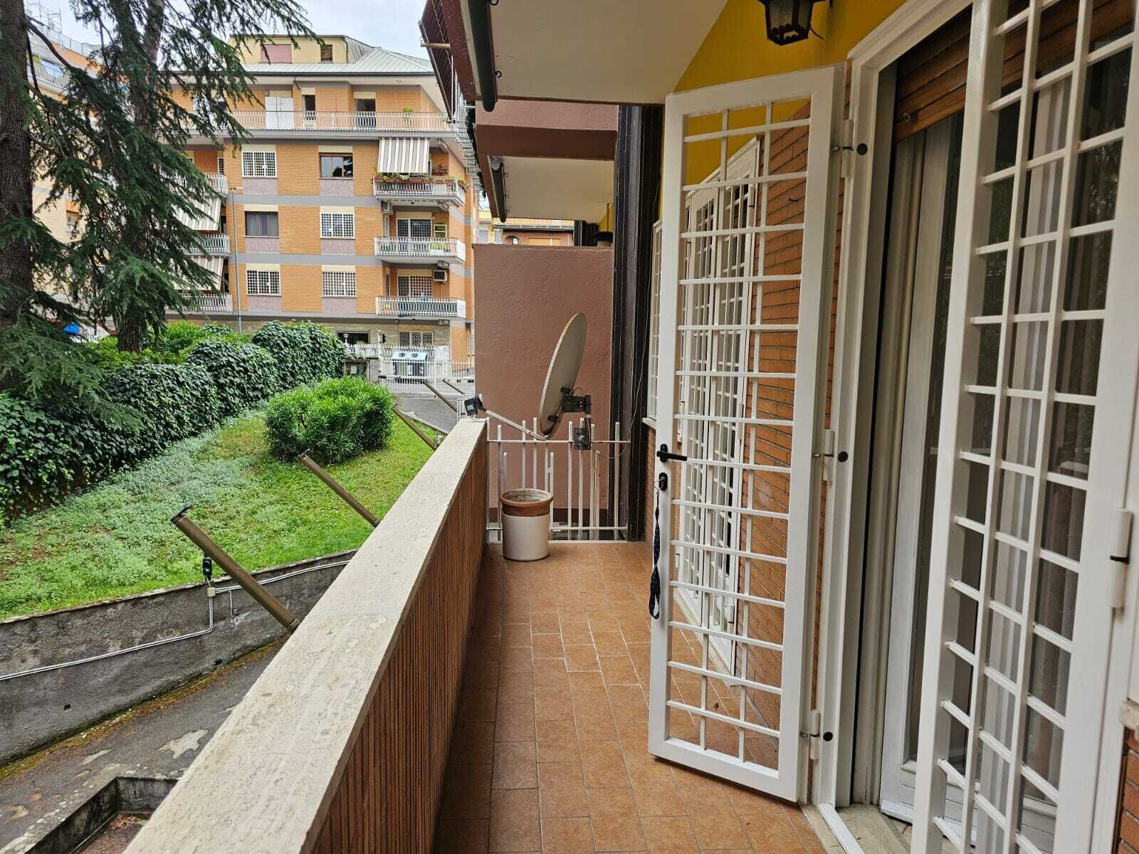 A balcony with a view of a residential area, a trash bin, and a door with a metal gate.