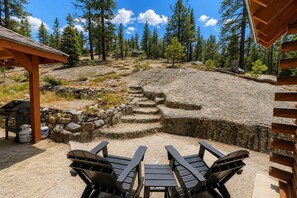 Eine Terrasse mit Adirondack-Stühlen, einem Grill und einer Steinmauer.