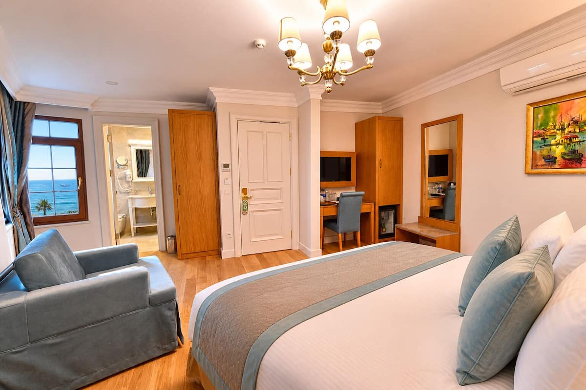 A hotel room with a bed, a desk, a chair, a mirror, and a view of the sea.