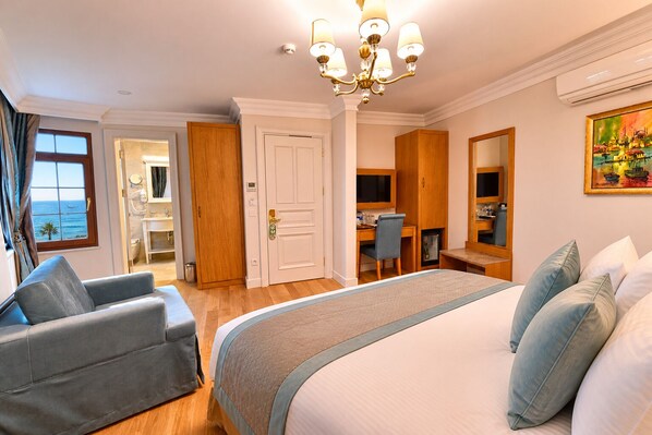 A hotel room with a bed, a desk, a chair, a mirror, and a view of the sea.