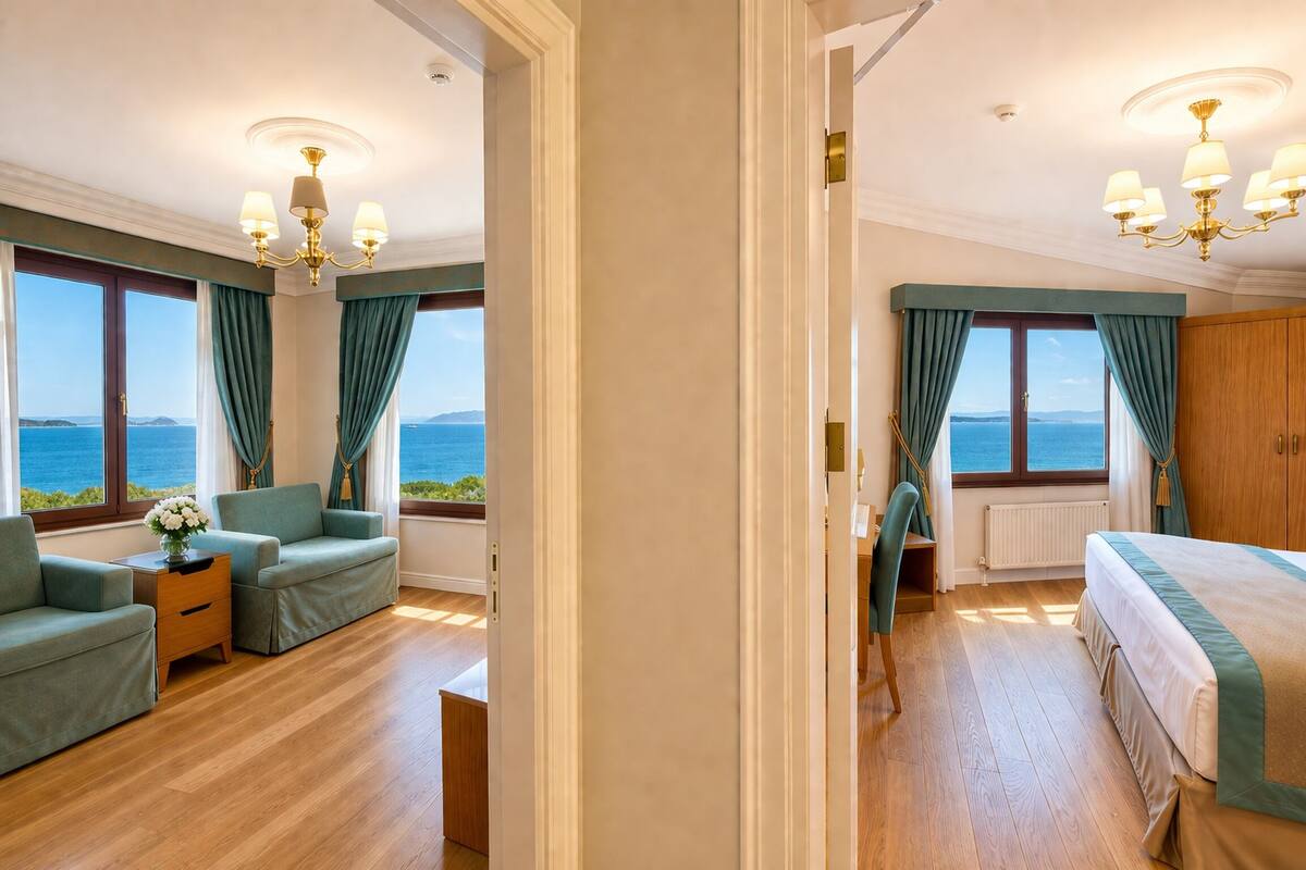 A hotel room with a bed, two sofas, a nightstand, a chair, and a view of the sea.