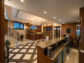 Un vestíbulo de hotel con una imponente escalera, una recepción, una zona de bar y un candelabro.