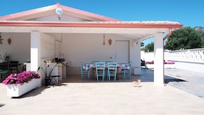 A covered outdoor seating area with a table and chairs, a potted plant, and a small dog. - Villa with Private Pool in Sardinia - Relax & Privacy (Quartu Sant'Elena)