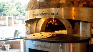 Kivilaatoilla päällystetty pizzauuni, jossa on digitaalinen näyttö, verkkosivuston logo ja pizzan kuva uunin sisällä.