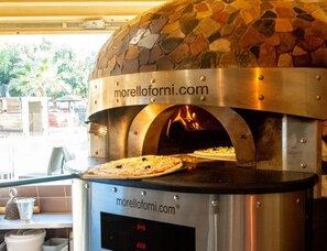 A stone-tiled pizza oven with a digital display, a website logo, and a pizza inside. - Beach Escape With Pool Access (Hyères)