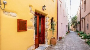 A narrow cobblestone alley with a yellow building featuring a wooden door and a potted plant. - Maisonette in center of Chania with roofgarden! (Chania)