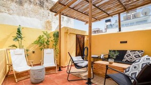 A patio with a wooden pergola, two white lounge chairs, a black sofa, and a small table. - Maisonette in center of Chania with roofgarden! (Chania)