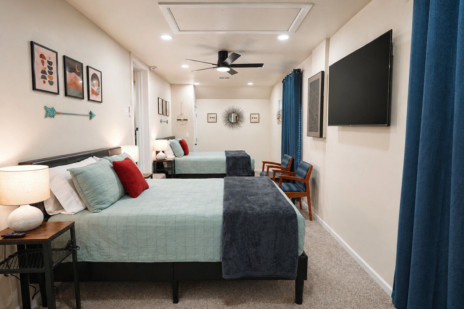 A hotel room with two beds, a ceiling fan, a flat-screen TV, and artwork on the walls.