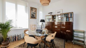 Et moderne spiseområde med et glasbord, træstole, en bogreol og en potteplante.
