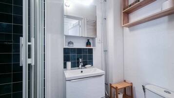 Une salle de bain avec un lavabo blanc, un miroir, un petit tabouret en bois et un espace douche.