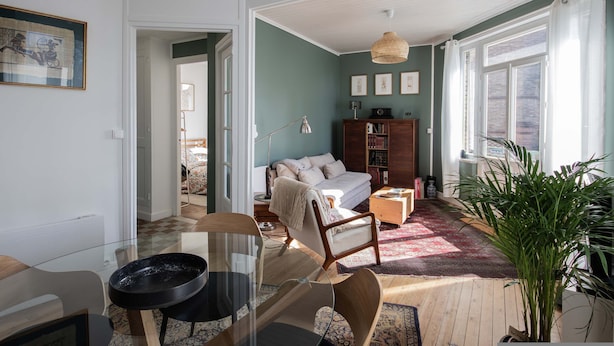En stue med sofa, sofabord, reol og et stort vindue.